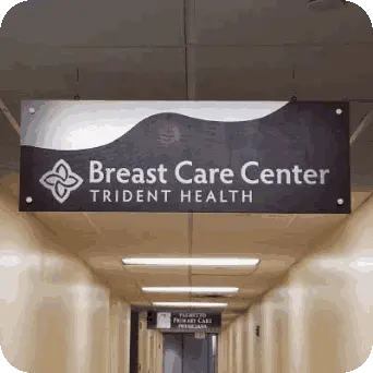 Hanging indoor metal sign with dark wood wavy mid-section. Text reads: Breast Care Center, Trident Health